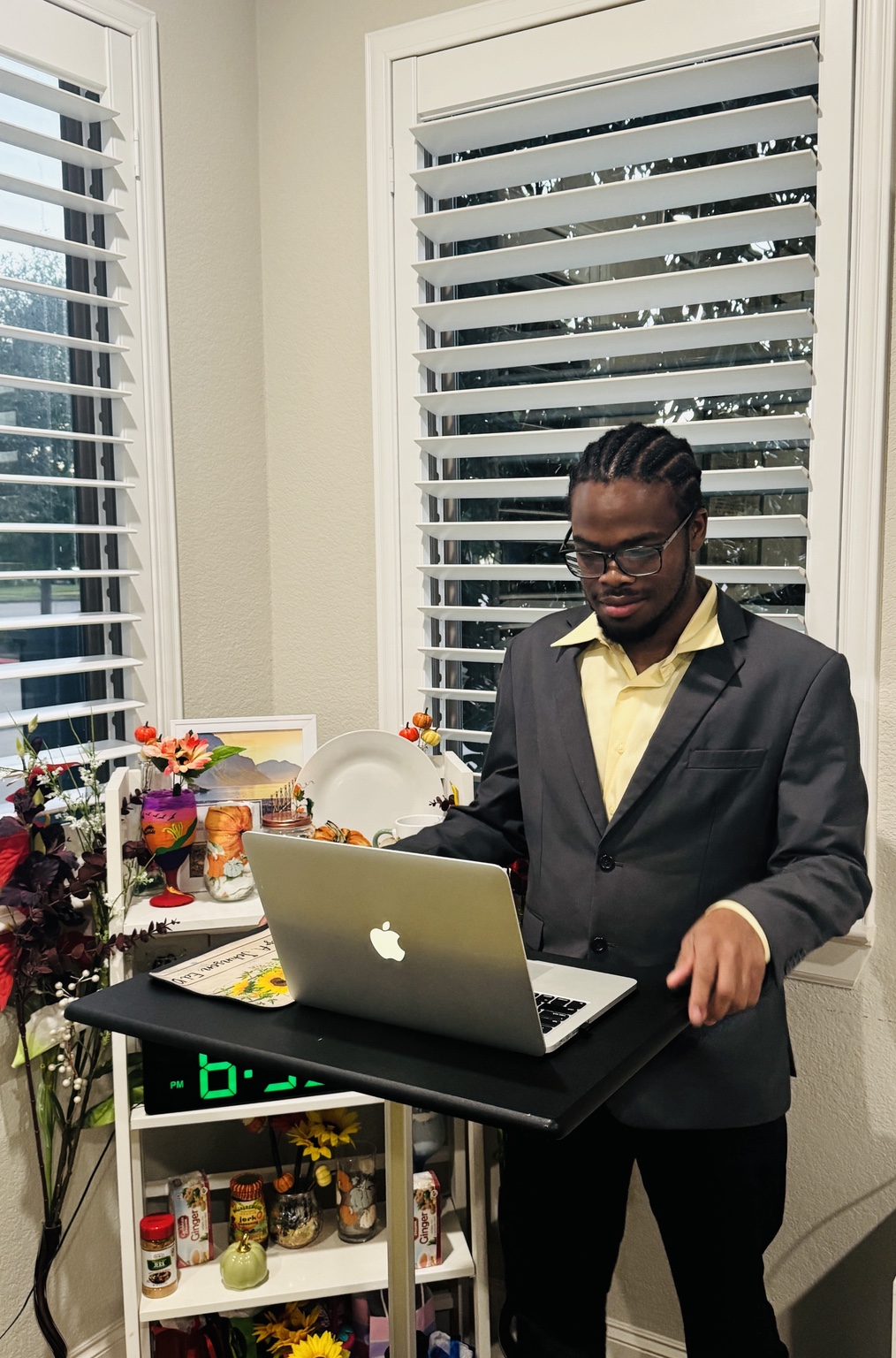 A presenter in a gold shirt and dark jacket speaking at a lectern with a laptop