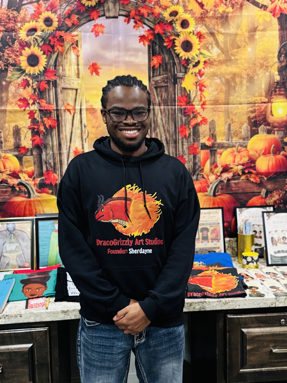 A smiling man in a black hoodie standing in front of an autumn floral display