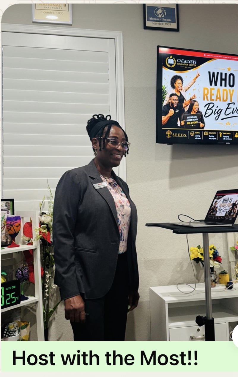 A woman in a dark suit standing beside a lectern and screen, captioned "Host with the Most!!"